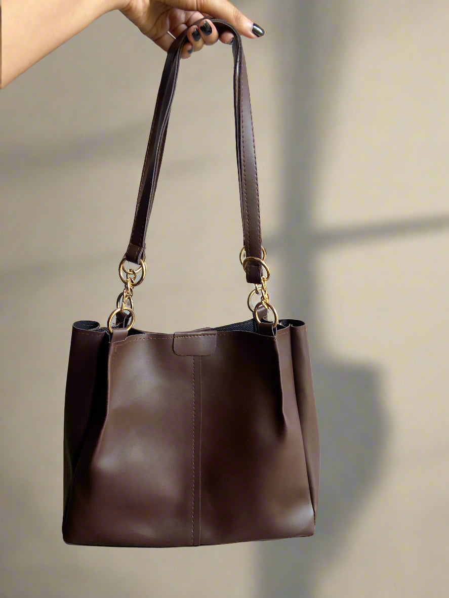 Brown leather handbag held by a hand against a neutral background