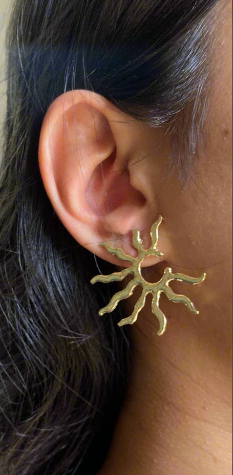 A gold sun-shaped earring with a blurred background.