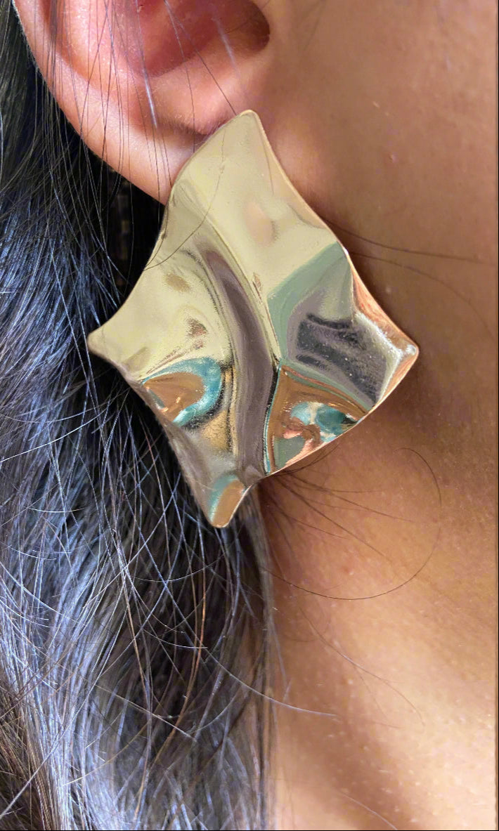Gold marbled earring worn on an ear with hair in the foreground