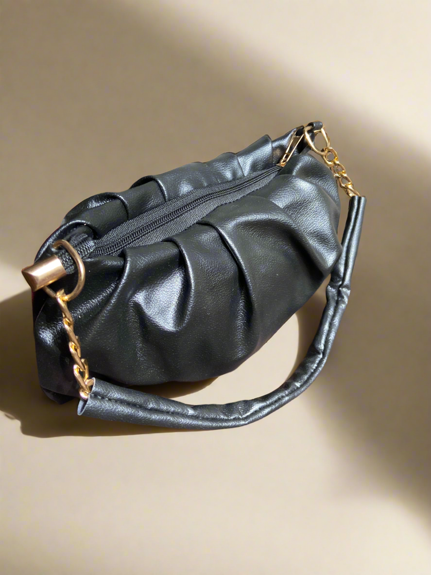 Black handbag with gold chain detail on a beige background