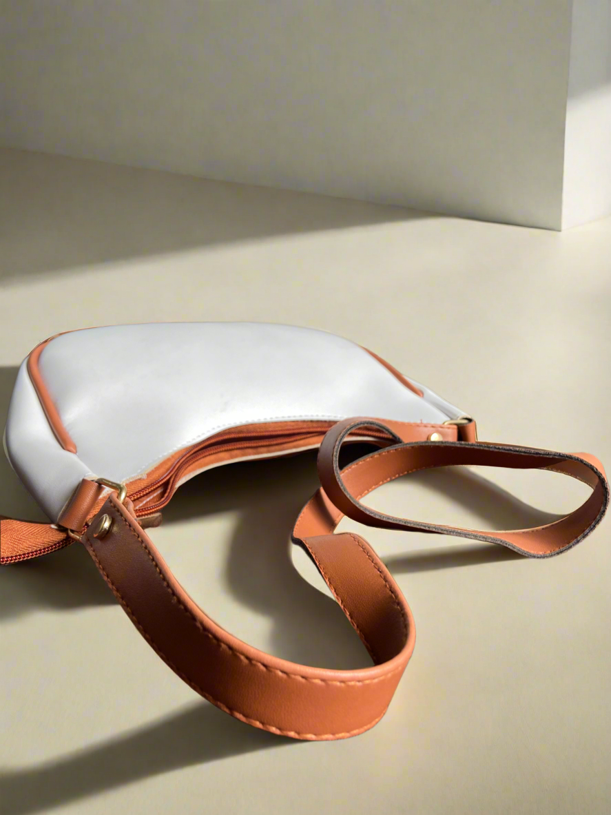 White handbag with brown leather strap on a beige surface