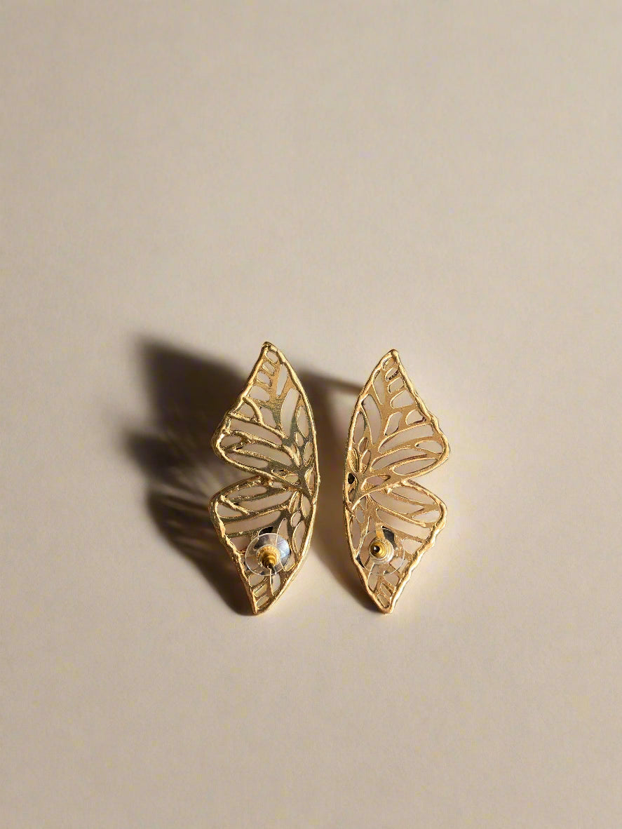 Two gold butterfly-shaped earrings on a black textured surface