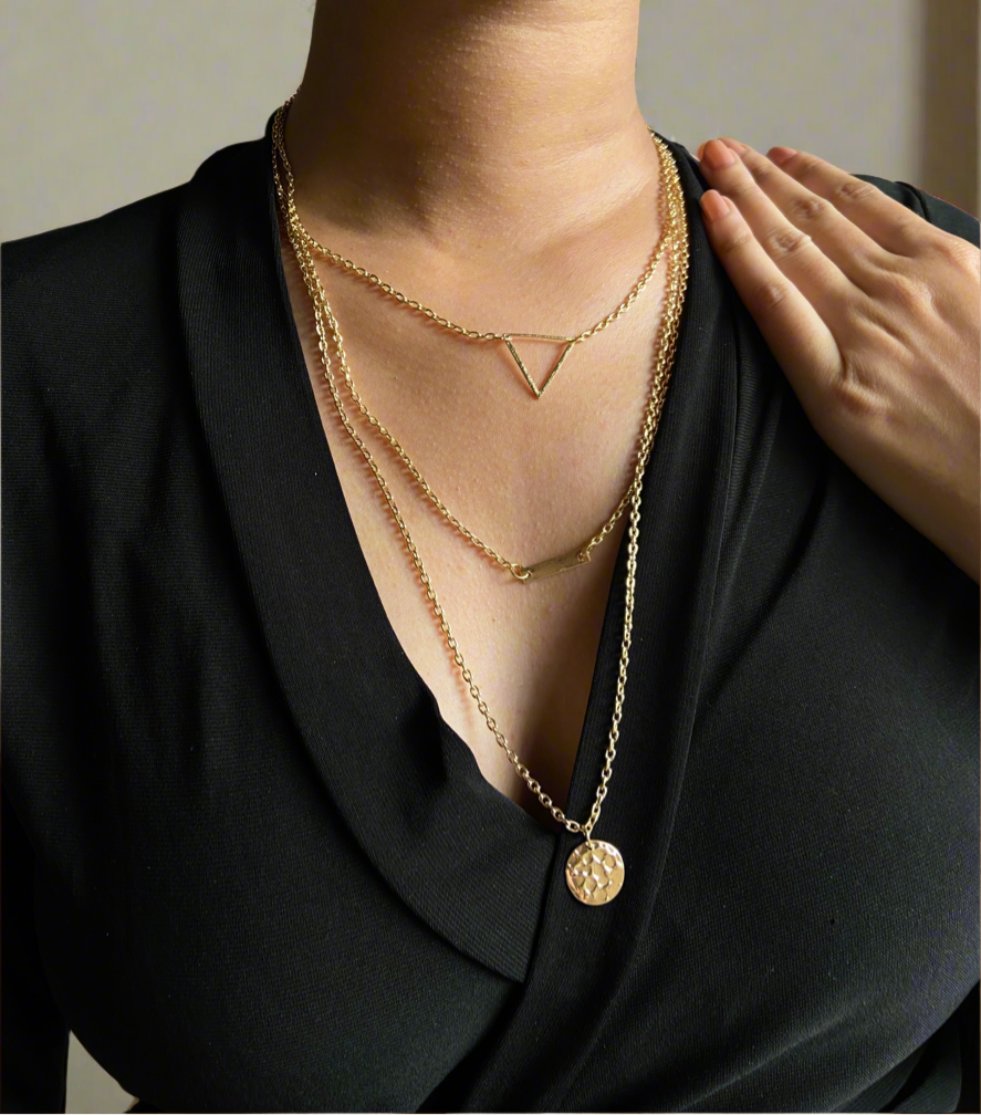 Gold necklace with a triangle pendant and circular charm on a black outfit.