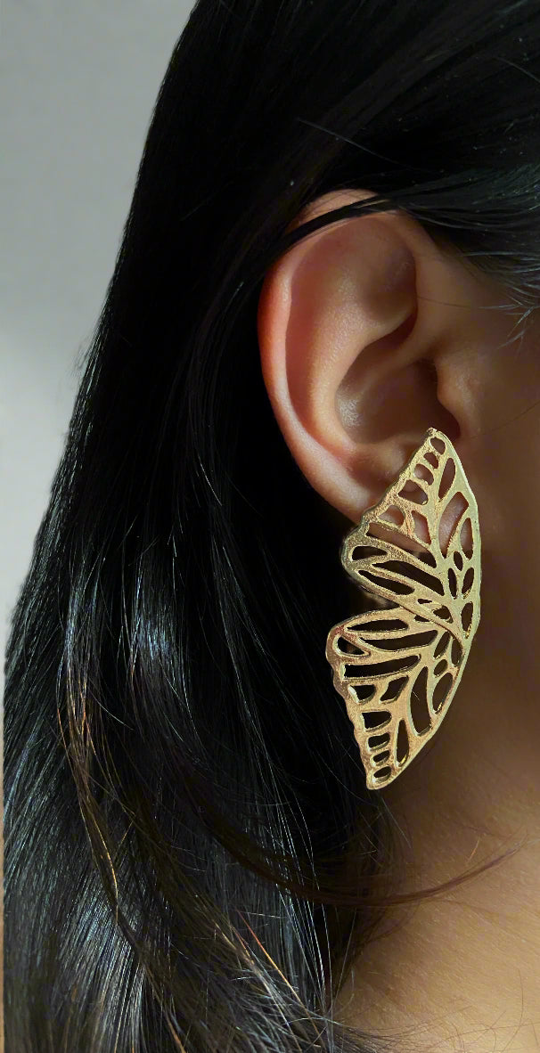 Gold leaf-shaped earring worn by a person with dark hair.