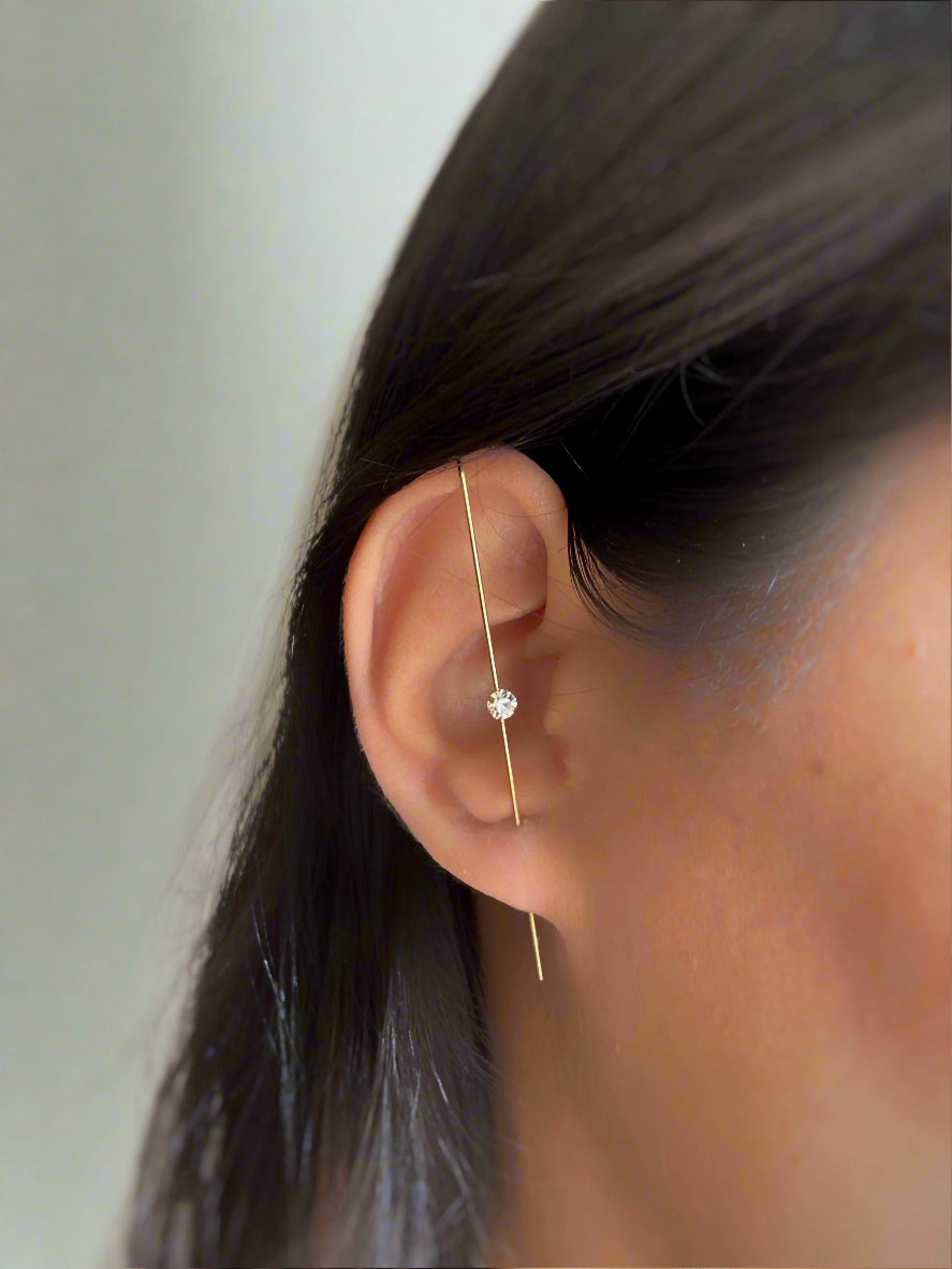 Close-up of an ear with a gold earring on a plain background
