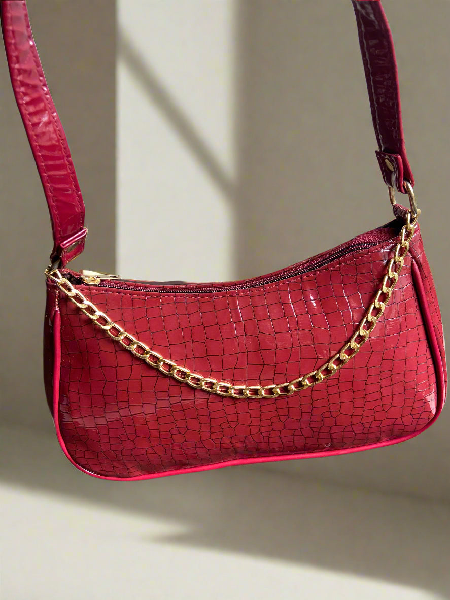 Red crocodile-patterned handbag with a gold chain strap against a neutral background