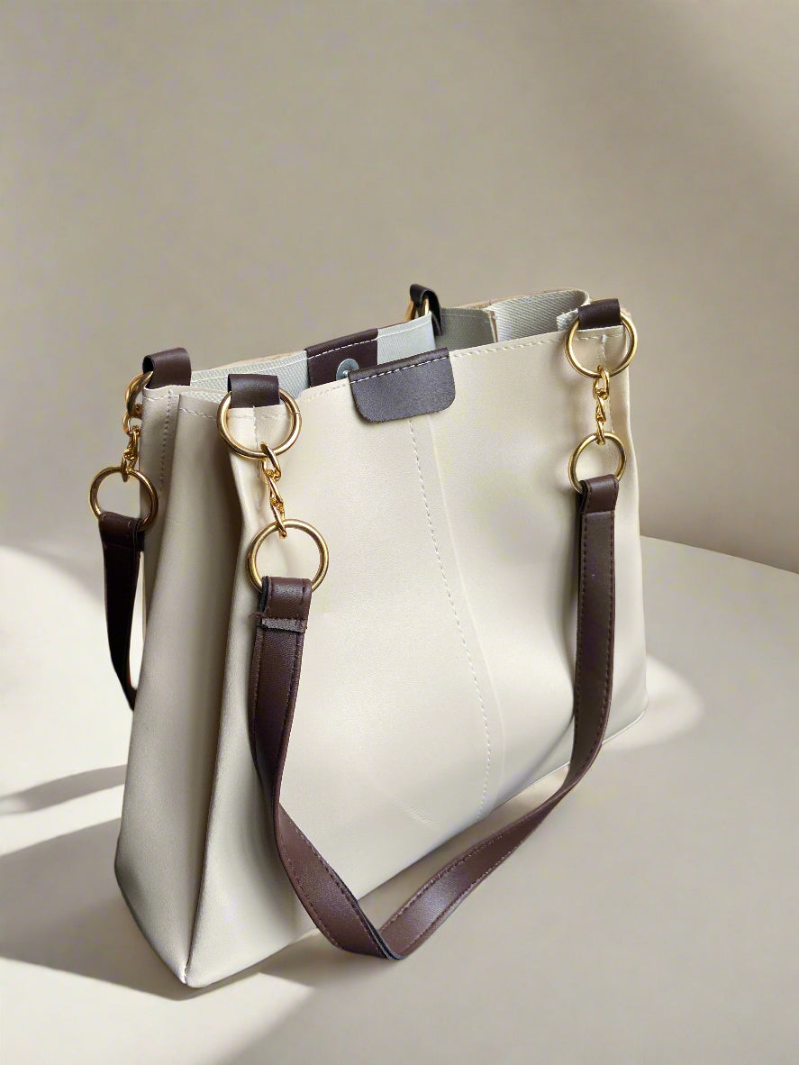 Beige handbag with brown strap and gold hardware on a textured surface