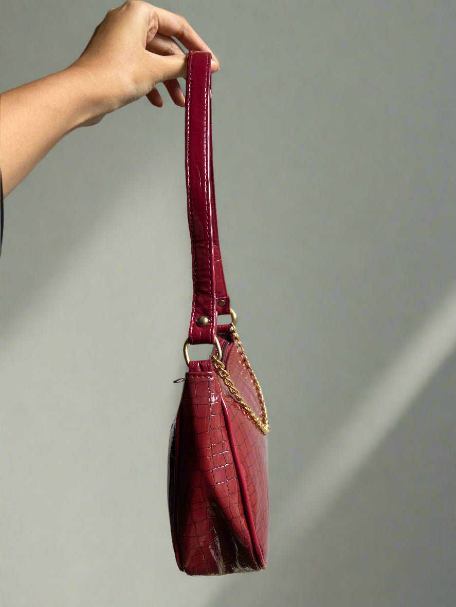 Red handbag with gold chain strap held by a hand against a gray background