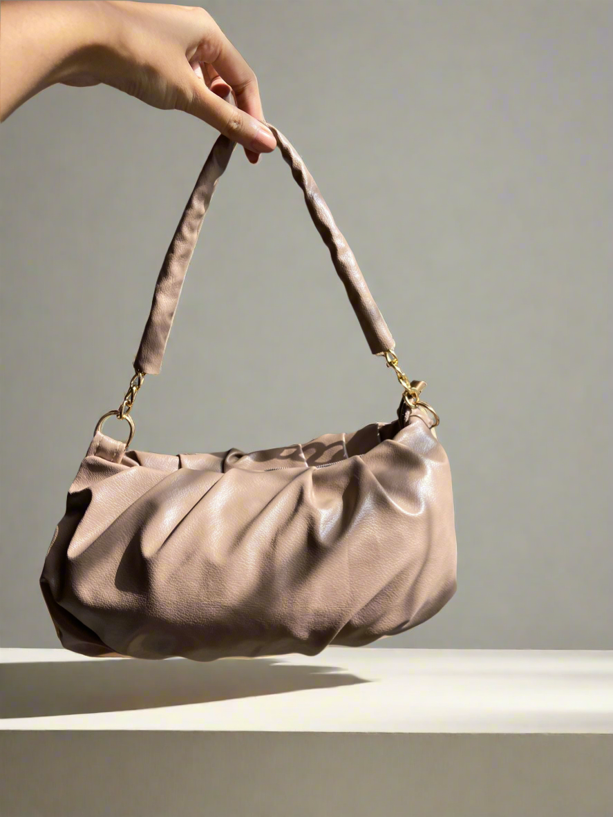 Hand holding a beige handbag against a neutral background