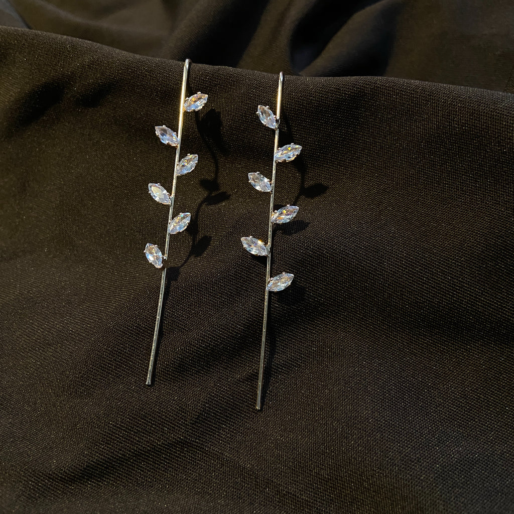 Pair of silver leaf-shaped earrings on a dark fabric background