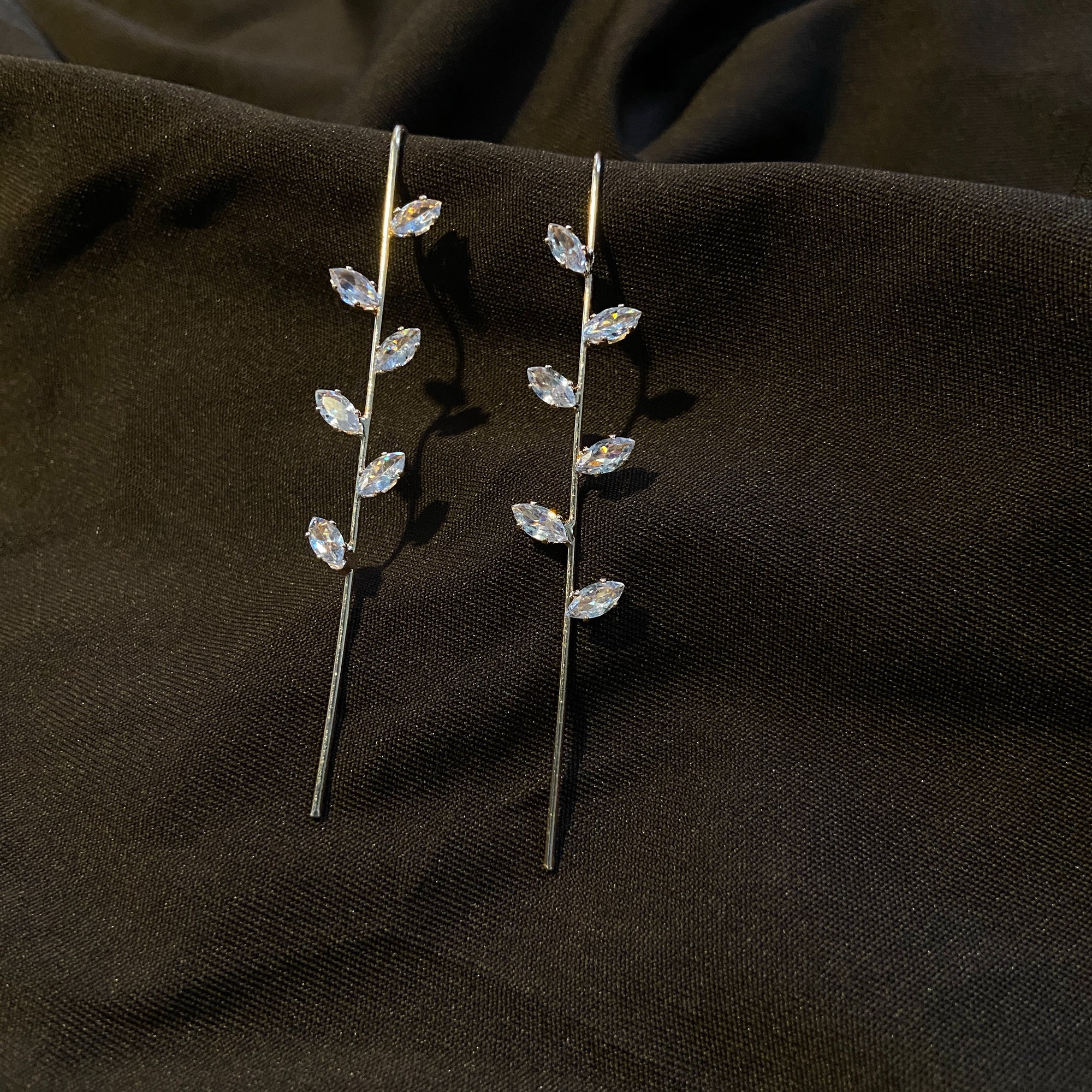 Pair of silver leaf-shaped earrings on a dark fabric background