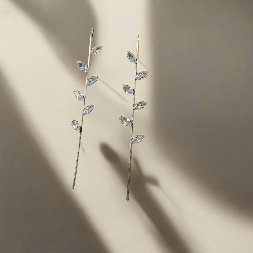 Pair of delicate earrings with crystal-like stones on a beige background