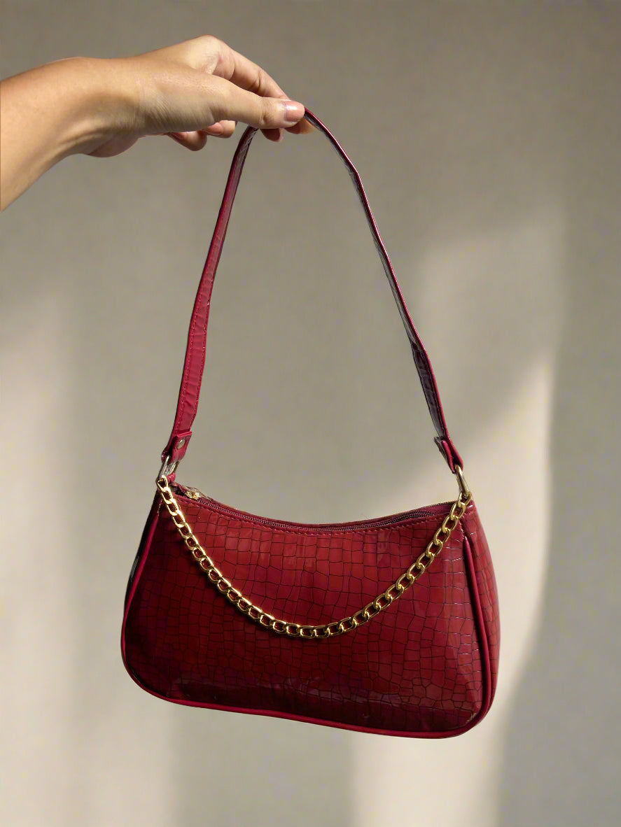 Red handbag with gold chain strap held by a hand against a gray background