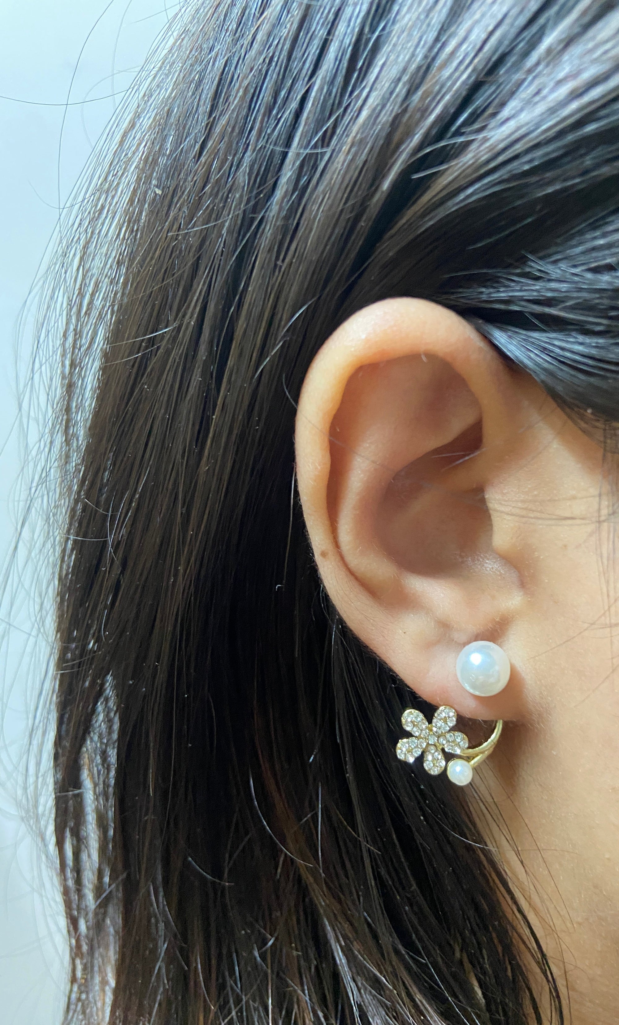 Close-up of an ear wearing a floral earring with pearl details.