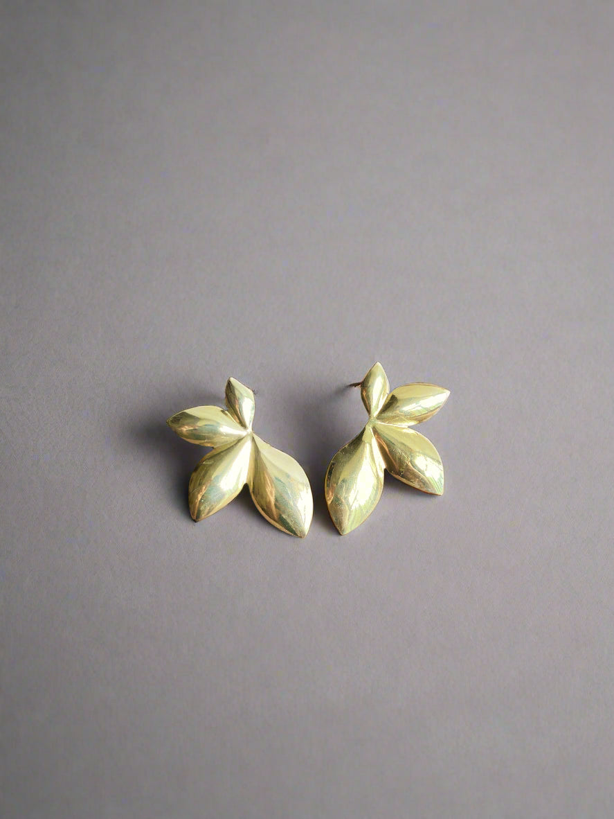Pair of gold leaf-shaped earrings on a dark fabric background