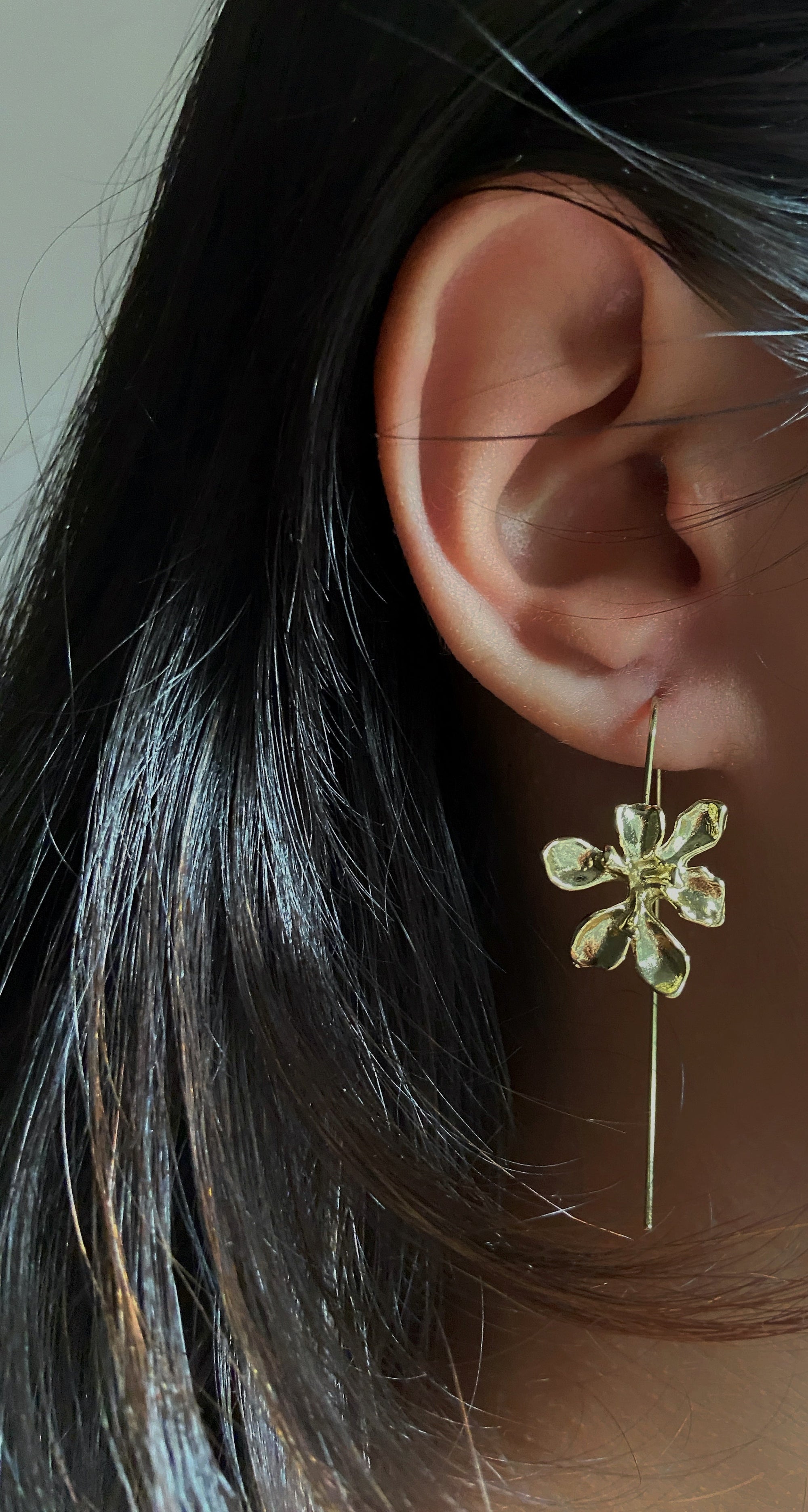 Close-up of an ear wearing a gold flower-shaped earring 
