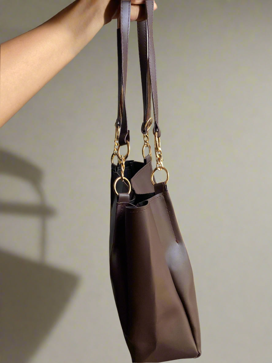 Brown handbag with gold accents held by a person against a neutral background