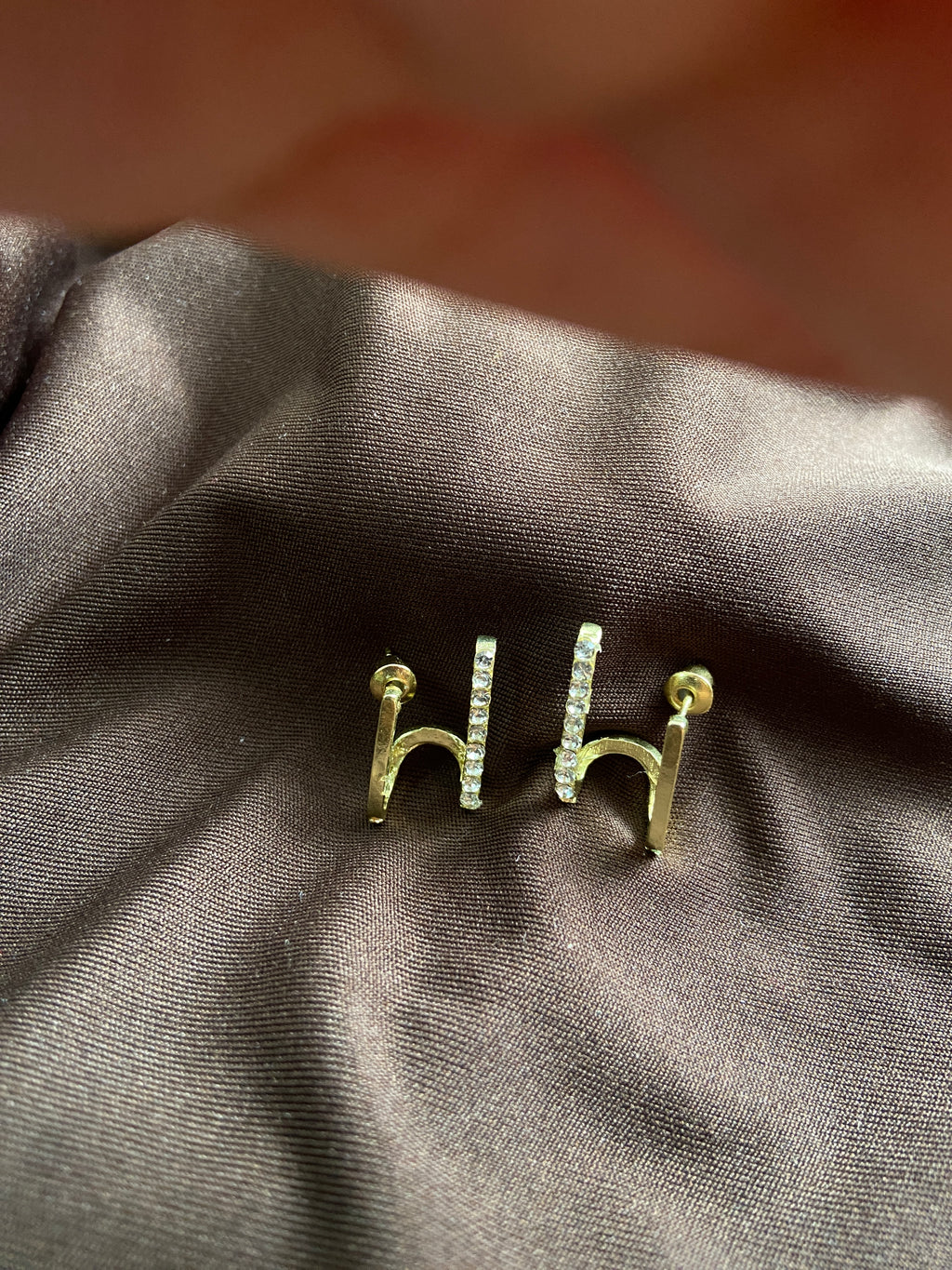 Gold bar earrings on a dark fabric background