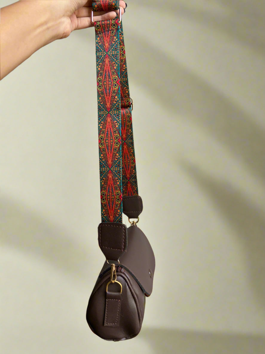 Brown leather bag with a patterned strap held by a hand against a neutral background