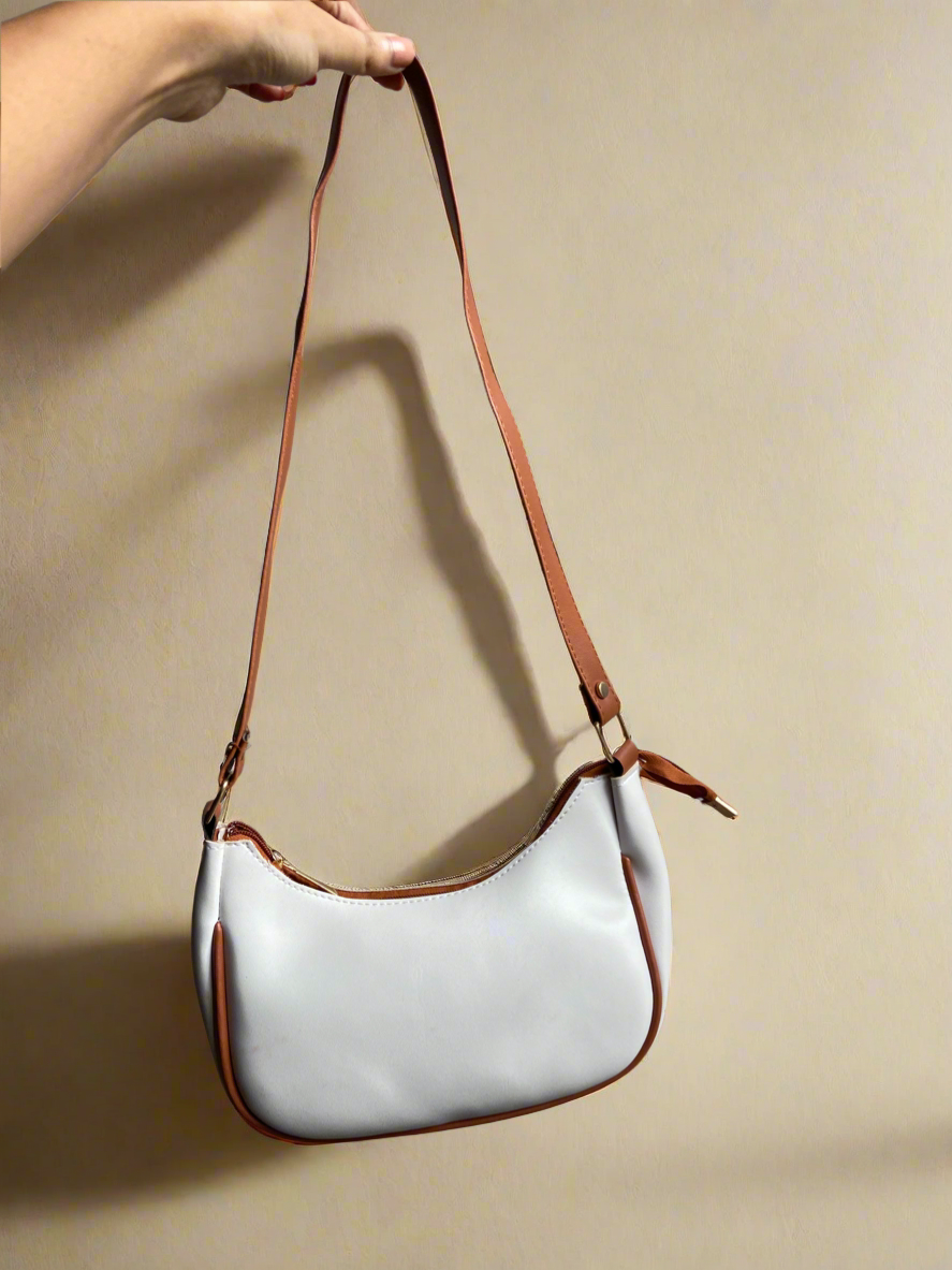White handbag with brown strap held by a hand against a beige background