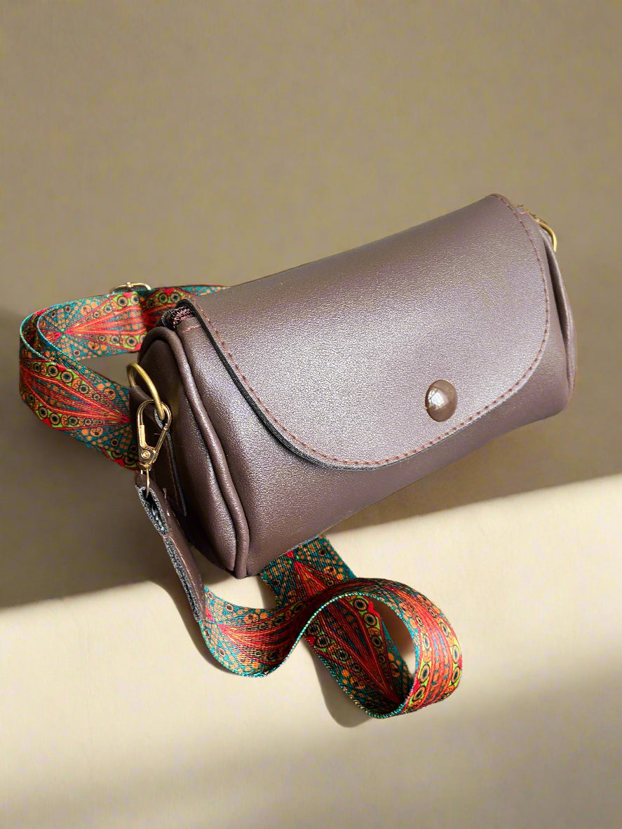 Brown boho bag with a colorful strap on a beige surface