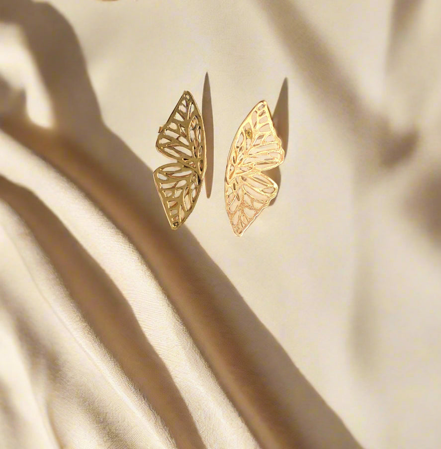 Gold butterfly-shaped earrings on a black textured surface