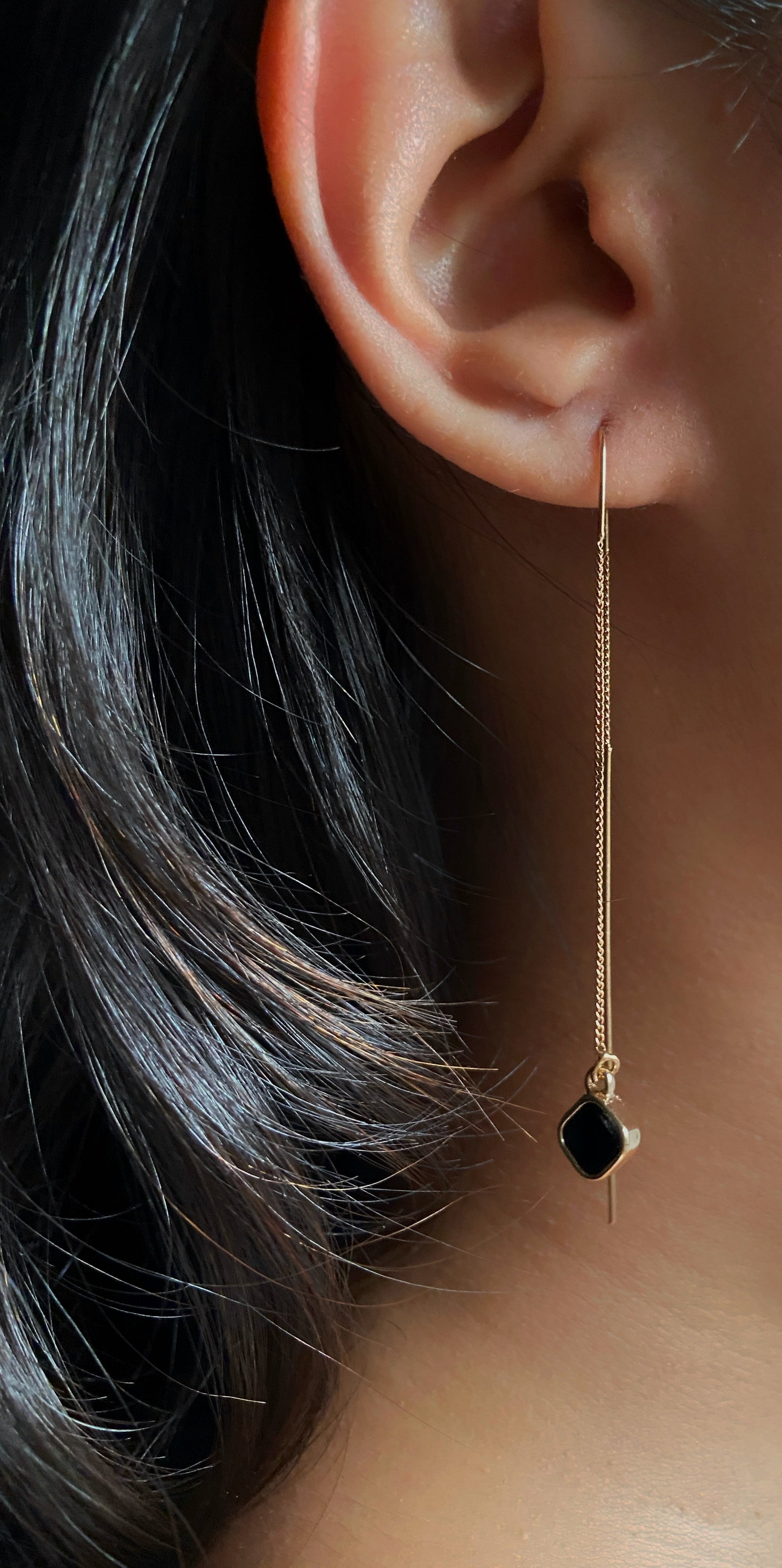 Close-up of an ear wearing a gold earring with a black gemstone.