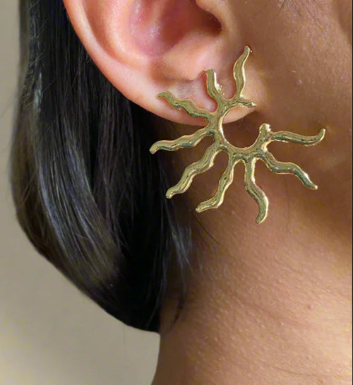 Gold sun-shaped earring worn by a person with a blurred background