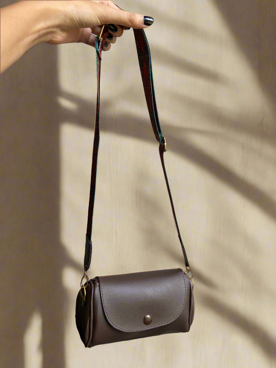 Brown leather handbag with a strap held by a hand against a beige background